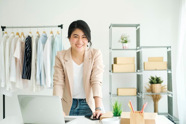 Heureuse jeune femme asiatique freelan debout dans un magasin de vêtements en ligne