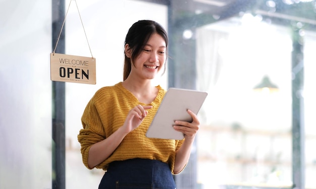 Heureuse jeune femme asiatique propriétaire debout tenant une tablette avec panneau ouvert