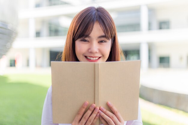 Heureuse jeune femme asiatique séduisante aime lire son livre à l'extérieur de son immeuble de bureaux