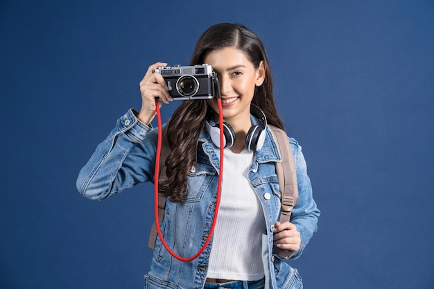 Heureuse jeune femme asiatique tenant et prenant une photo avec un appareil photo vintage sur fond de couleur bleu