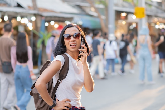 Heureuse jeune femme asiatique de voyage à l'aide de téléphone mobile sur un marché de rue.