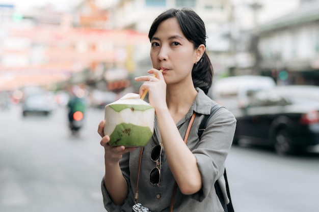 Heureuse jeune femme asiatique voyageur sac à dos buvant un jus de noix de coco au marché de l'alimentation de rue de la ville chinoise à Bangkok en Thaïlande Voyageur vérifiant les rues latérales