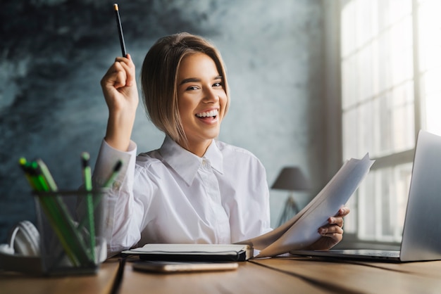 Heureuse jeune femme assise au bureau et étudie