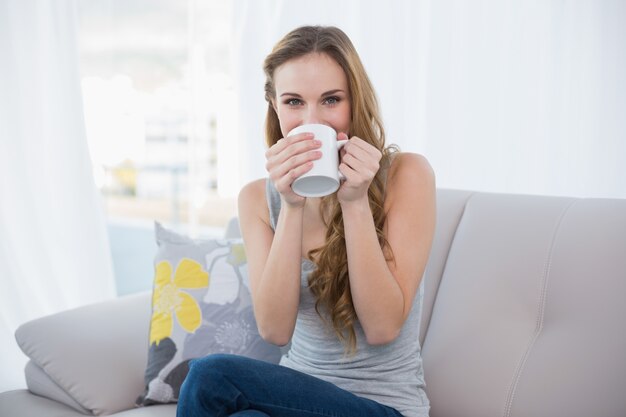 Heureuse jeune femme assise sur un canapé à boire dans une tasse