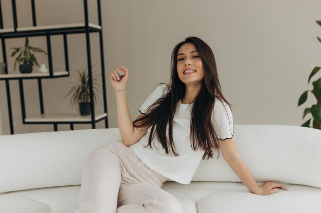 Heureuse jeune femme assise sur un canapé à la maison et regardant la caméra