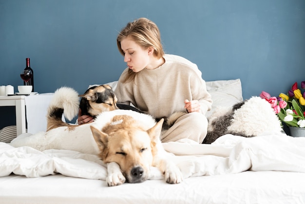 Heureuse jeune femme assise dans le lit avec ses chiens, fond de mur bleu