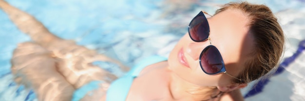 Heureuse jeune femme assise dans la piscine portant des lunettes à la mode