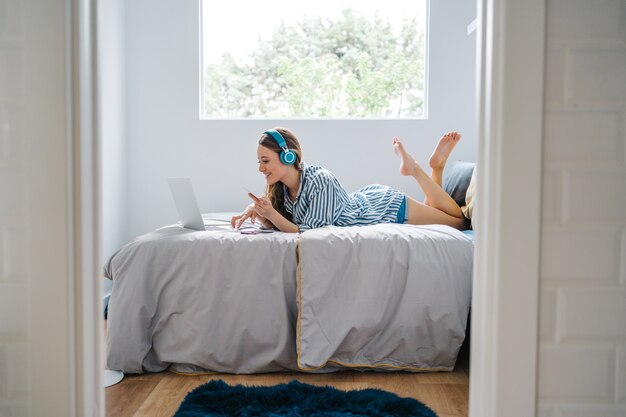 heureuse jeune femme assise dans sa chambre naviguant sur un téléphone intelligent tout en écoutant de la musique