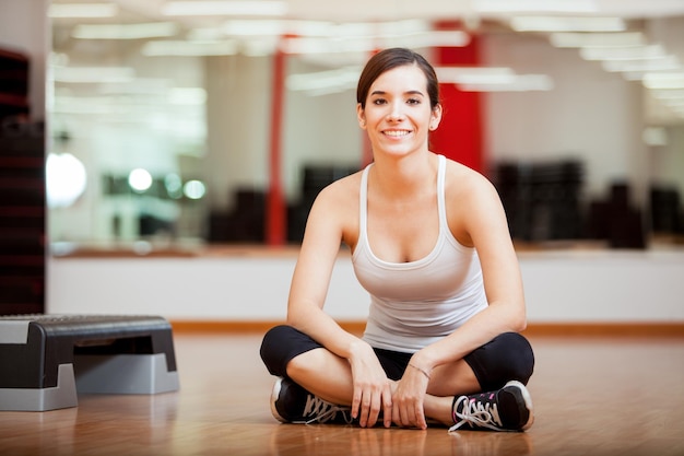 Heureuse jeune femme assise dans une salle de sport et se préparant pour un cours