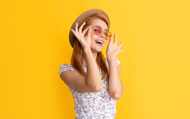 Heureuse jeune femme au chapeau de paille et lunettes de soleil sur fond jaune