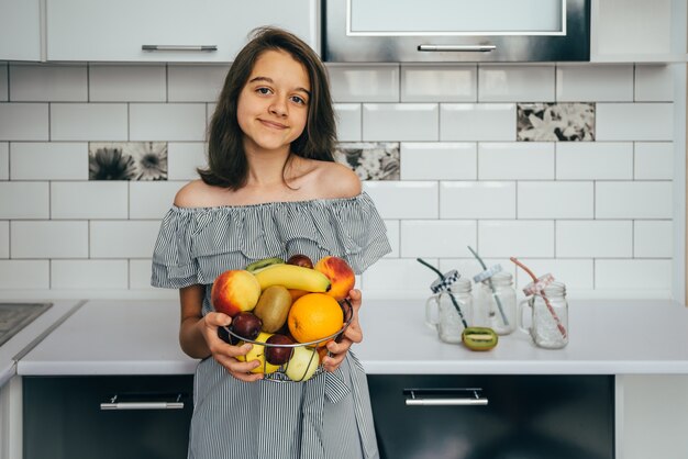 Heureuse jeune femme au foyer avec des fruits dans une cuisine moderne.