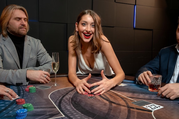 Heureuse Jeune Femme Aux Cheveux Bruns Excitée Assise à Une Table De Poker Dans Un Casino, Ratissant Une Pile De Jetons Gagnés Satisfaite D'un Jeu Réussi. Concept De Passion Pour Le Jeu