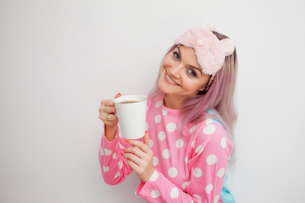 Heureuse jeune femme boit du café du matin. Belle fille en pyjama rose et masque de nuit