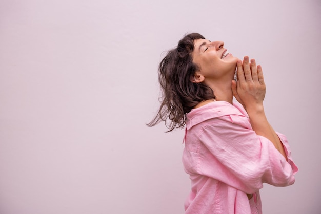 Heureuse jeune femme brune caucasienne aux yeux fermés tient les paumes ensemble sur fond avec un espace pour le texte Concept de loisirs de différentes émotions de style de vie