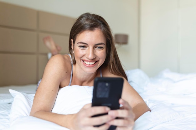 Heureuse jeune femme brune utilisant un téléphone portable à la maison Belle fille surfer sur le net sur smartphone