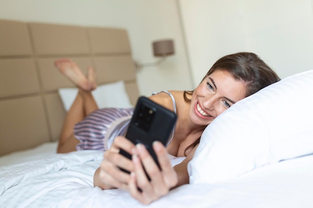 Heureuse jeune femme brune utilisant un téléphone portable à la maison Belle fille surfer sur le net sur smartphone