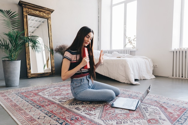 Heureuse jeune femme cadeau d'ouverture devant un ordinateur portable lors d'un appel vidéo ou d'un chat, célébrant l'anniversaire en ligne.