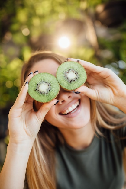 Heureuse jeune femme caucasienne tenant le kiwi devant les yeux