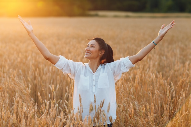 Heureuse jeune femme sur champ de blé avec les mains levées jouissant de la liberté