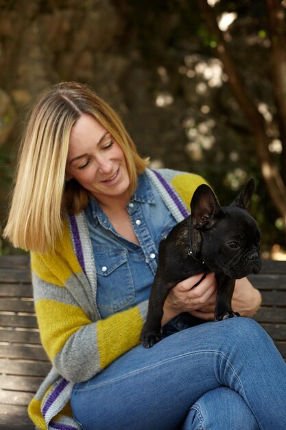 Heureuse jeune femme avec chien bouledogue français assis sur un banc en plein air