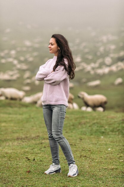 Heureuse jeune femme dans un pull contre des troupeaux de moutons dans les montagnes