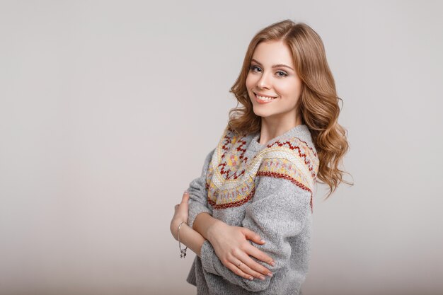 Heureuse jeune femme dans un pull élégant à la mode sur fond gris