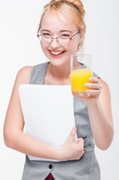 Heureuse jeune femme dans des verres souriant à la caméra et tenant un verre de jus d'orange frais. Émotions positives, énergie, beauté