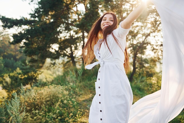 Heureuse jeune femme dansant avec un chiffon blanc dans les mains à l'extérieur dans la forêt