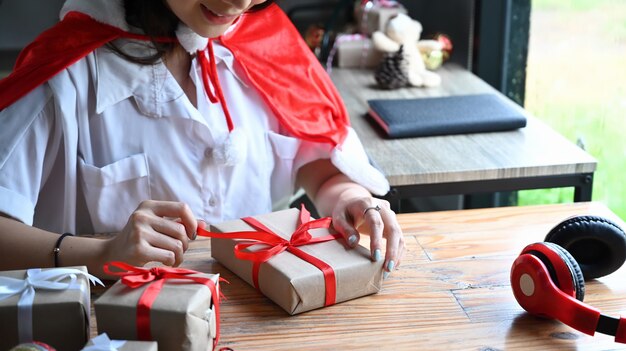 Heureuse jeune femme décorant un cadeau de Noël avec un ruban rouge.