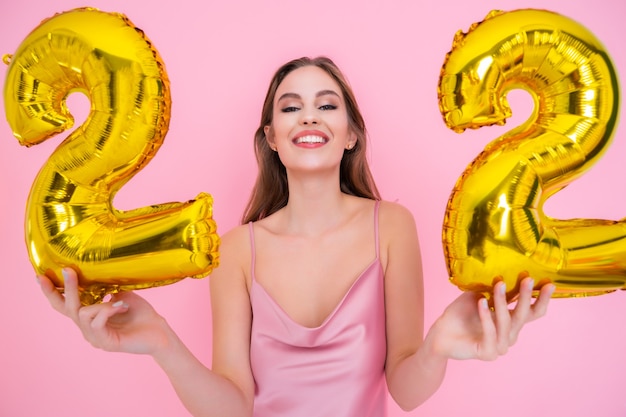 Heureuse jeune femme détient un ballon en feuille d'or isolé sur fond rose concept de fête d'anniversaire