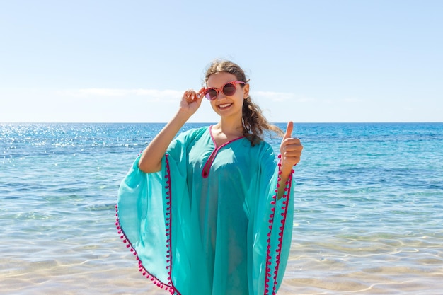 Heureuse jeune femme donnant le signe de la main pouce levé sur la plage