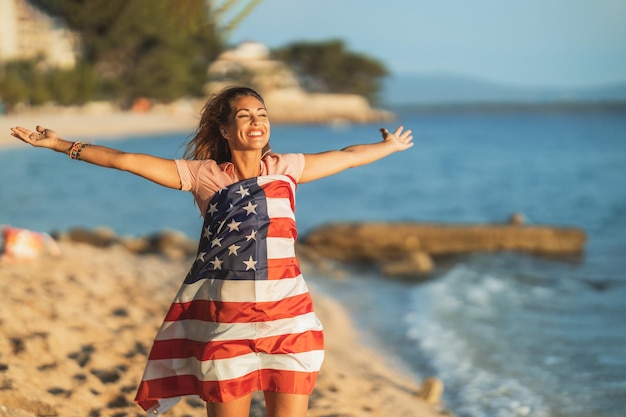 Photo heureuse jeune femme avec le drapeau national américain passant une journée de détente sur la plage.