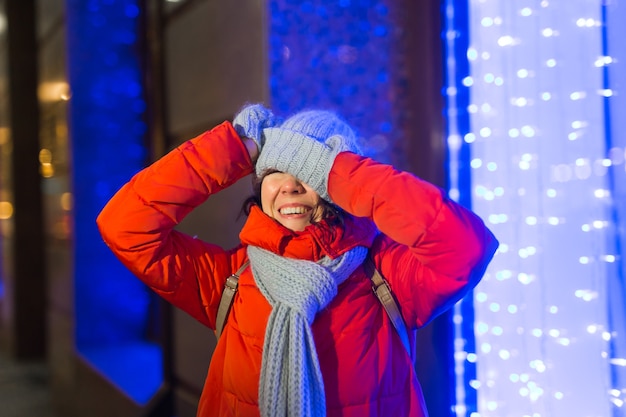 Heureuse jeune femme drôle avec des vêtements d'hiver fond soirée éclairage des lumières de la ville. Concept de vacances de Noël et d'hiver.