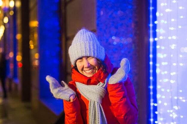 Heureuse jeune femme drôle avec des vêtements d'hiver fond soirée éclairage des lumières de la ville. Concept de vacances de Noël et d'hiver.