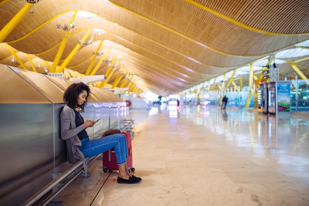 Heureuse jeune femme écoutant de la musique avec des écouteurs et un téléphone portable à l'aéroport