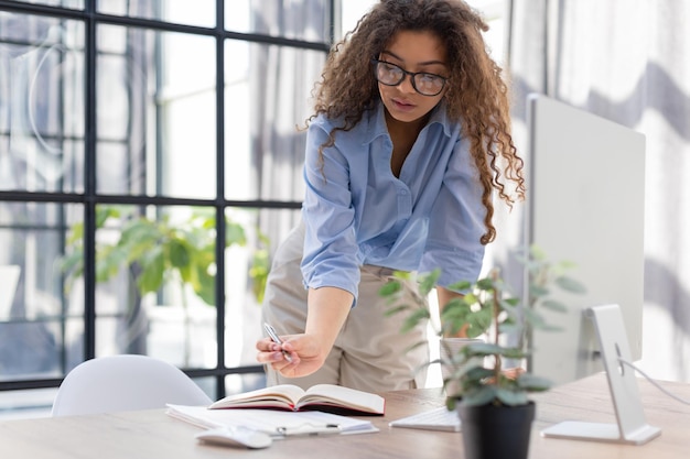 Heureuse jeune femme écrivant quelque chose tout en travaillant au bureau