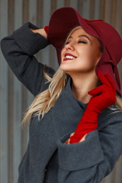 Heureuse jeune femme élégante dans un chapeau à la mode et un manteau élégant près d'un mur en bois gris. Bonne humeur