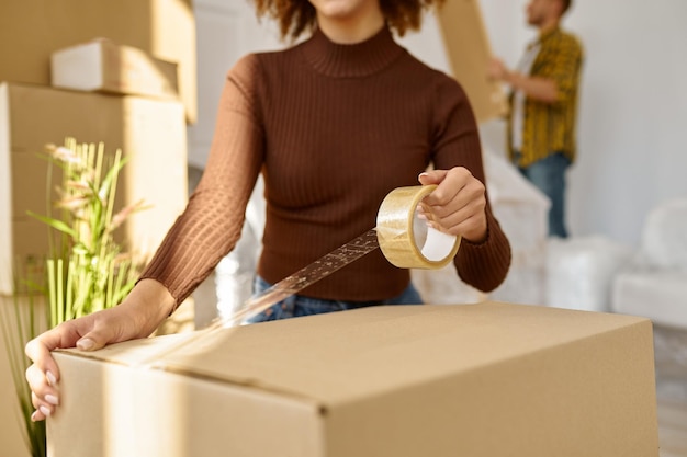 Heureuse jeune femme emballant une boîte en carton pour emménager dans un nouvel appartement à la maison debout dans le salon