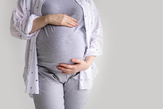 Heureuse jeune femme enceinte en pyjama serrant le ventre posant isolé sur blanc studio