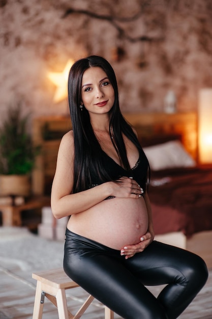 Heureuse Jeune Femme Enceinte En Soutien-gorge Noir élégant Et Boucle D'oreille Moderne Tenant La Bosse Du Ventre Et Posant En Photo De Mode Légère