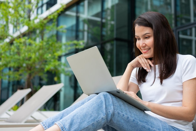 Heureuse jeune femme entrepreneur assise sur un lit de bronzage au bord de la piscine et utilisant un ordinateur portable