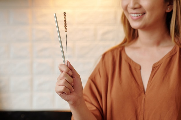 Heureuse jeune femme excitée tenant une paille en métal réutilisable et une petite brosse pour son nettoyage