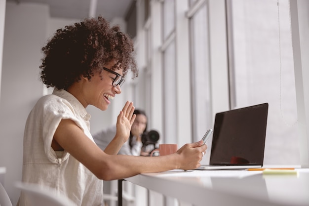 Heureuse jeune femme faisant un appel vidéo alors qu'elle était assise sur le lieu de travail