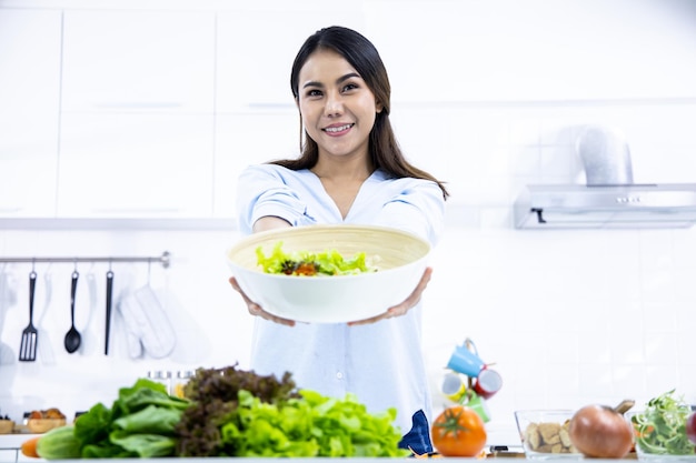 Heureuse jeune femme faisant une salade saine dans la cuisine à la maison avec le sourire. Alimentation saine à la maison. Concept de mode de vie sain.