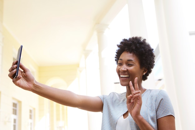 Heureuse Jeune Femme Gesticulant Un Signe De Paix Et Prenant Selfie