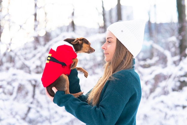 Heureuse jeune femme en hiver, tient dans ses bras et joue dans la neige avec son animal de compagnie, chien chihuahua