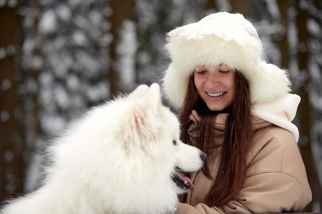 Heureuse jeune femme en hiver tient dans ses bras et joue dans la neige avec son chien de compagnie