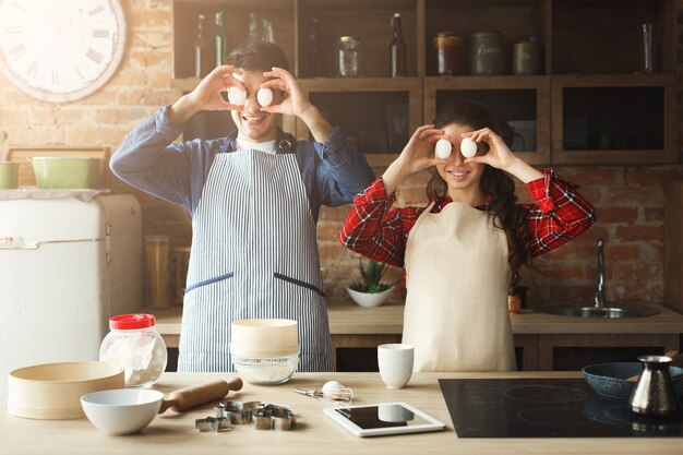 Heureuse jeune femme et homme faisant une tarte et s'amusant dans la cuisine loft. Jeune famille cuisinant à la maison, à l'aide d'une tablette numérique. Maquette pour la recette