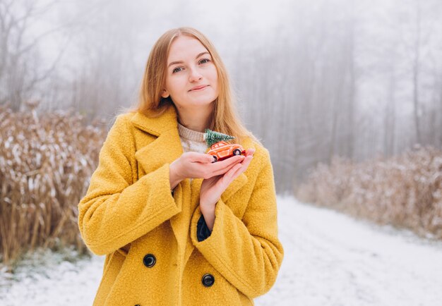 Heureuse jeune femme avec un jouet portant un manteau jaune souriant sur fond nature, couleur tendance de l'année 2021 - jaune illuminant, heure d'hiver