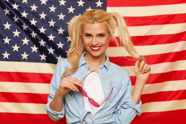 Heureuse jeune femme à lunettes de soleil en forme de coeur sur fond de drapeau USA.